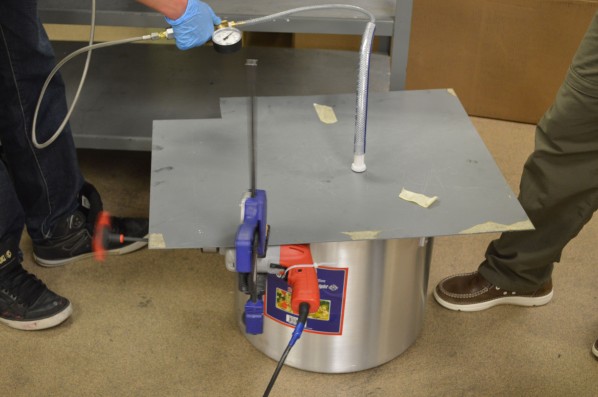 After it's mixed, the mixture is put into a big pot. Here the hose coming out of the metal plate is connected to a vacuum, and the orange handle belongs to a drill that is clamped onto the sheet to shake out air bubbles. Photo by Jake Lucas